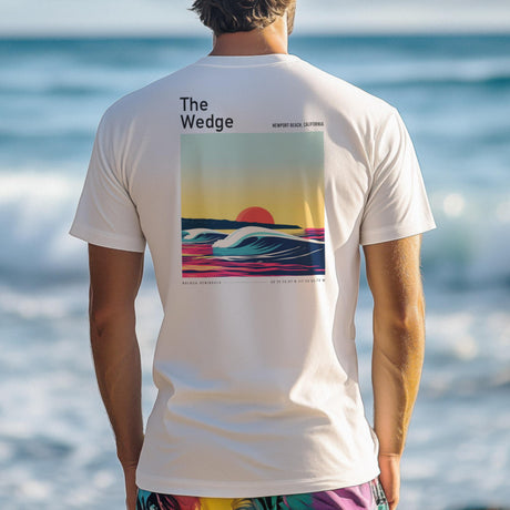 A person stands on the beach wearing a white shirt featuring a vibrant, retro-style poster of a wave at sunset, labeled The Wedge, Newport Beach, California. The shirt acts as striking wall art against the ocean backdrop.