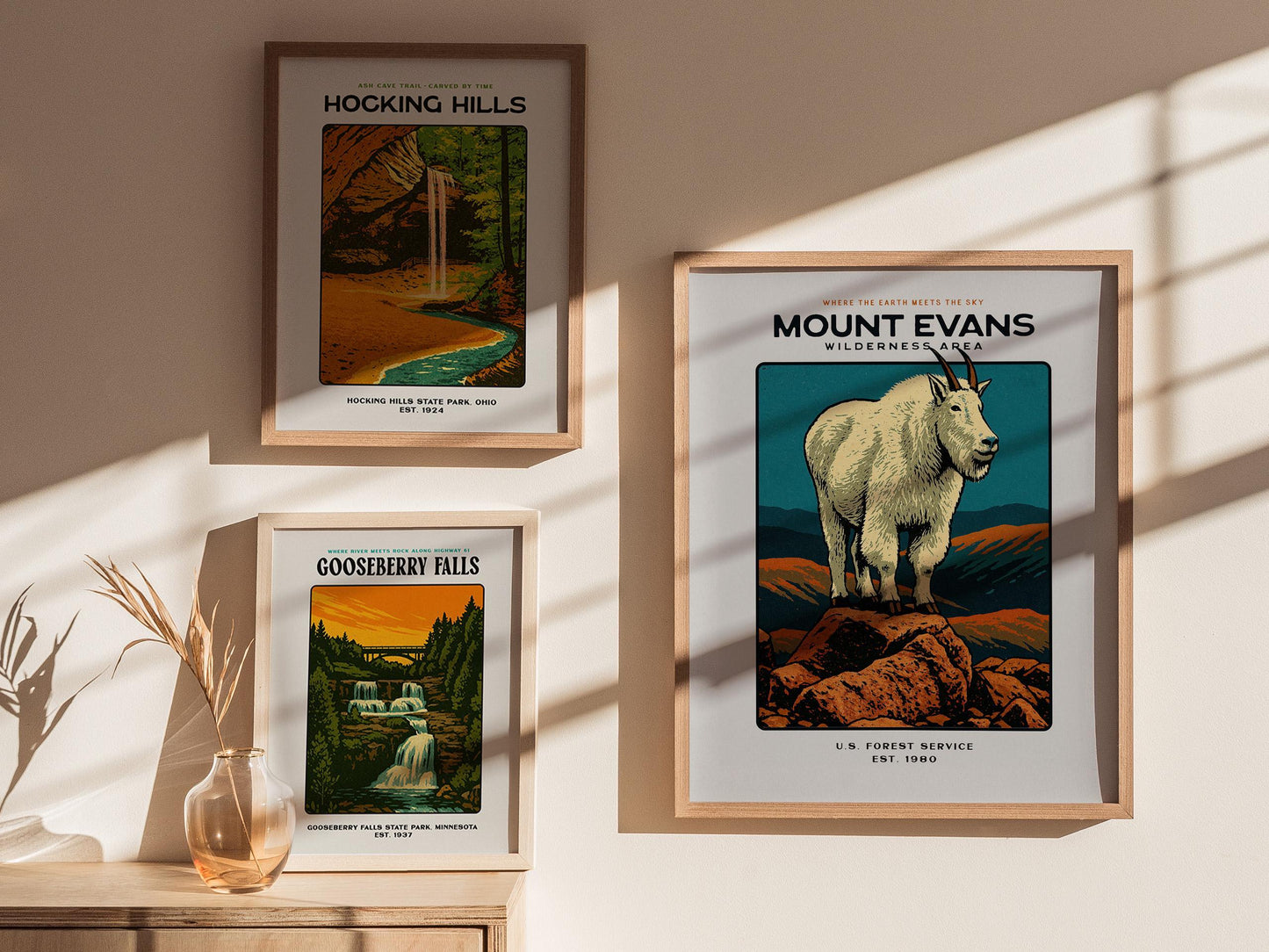 Three framed posters of natural landscapes on a wall with sunlight casting shadows.