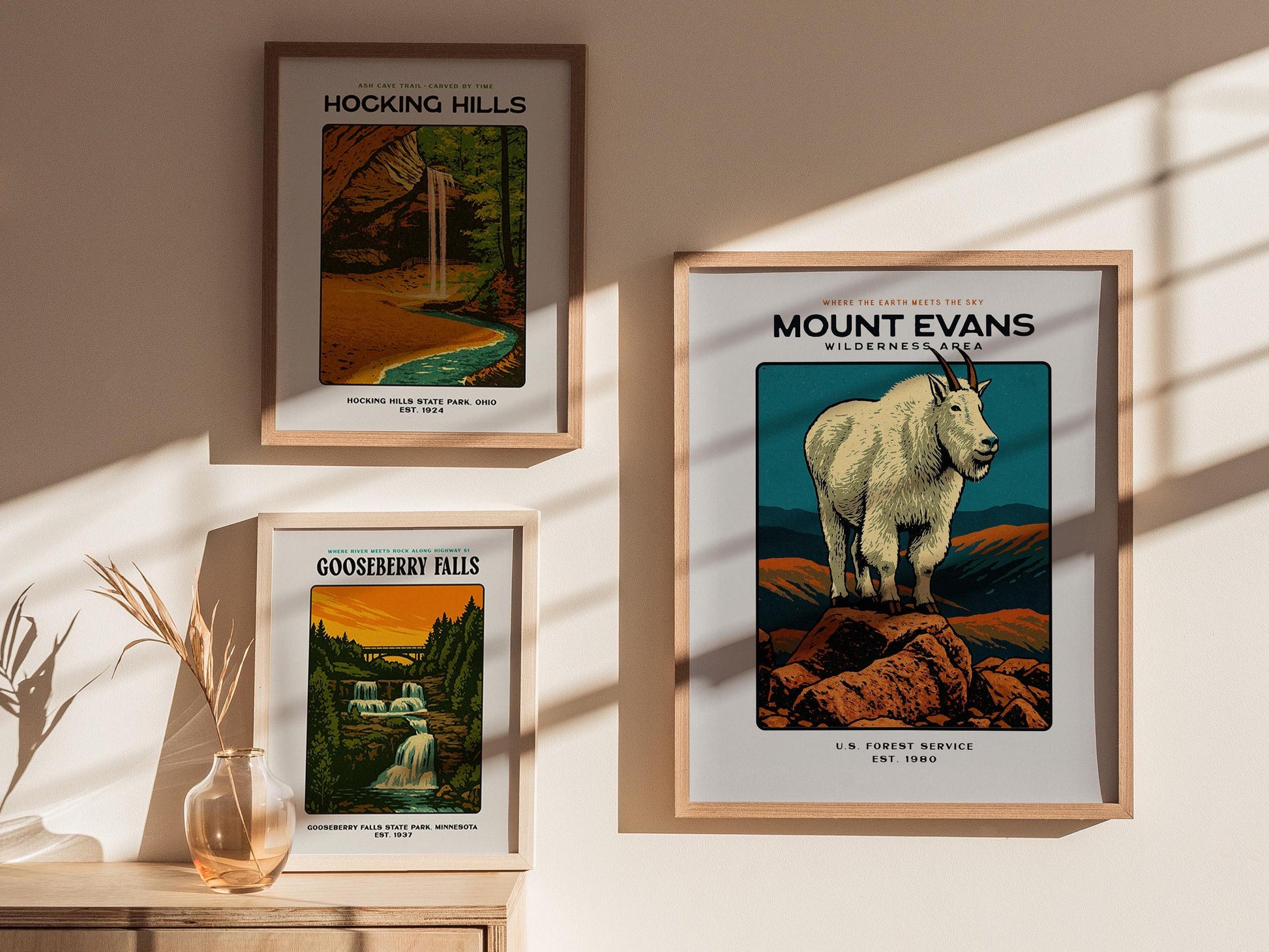 Three framed posters of natural landscapes on a wall with sunlight casting shadows.