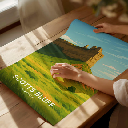 Person holding a scenic poster of Scotts Bluff, Nebraska on a wooden surface.