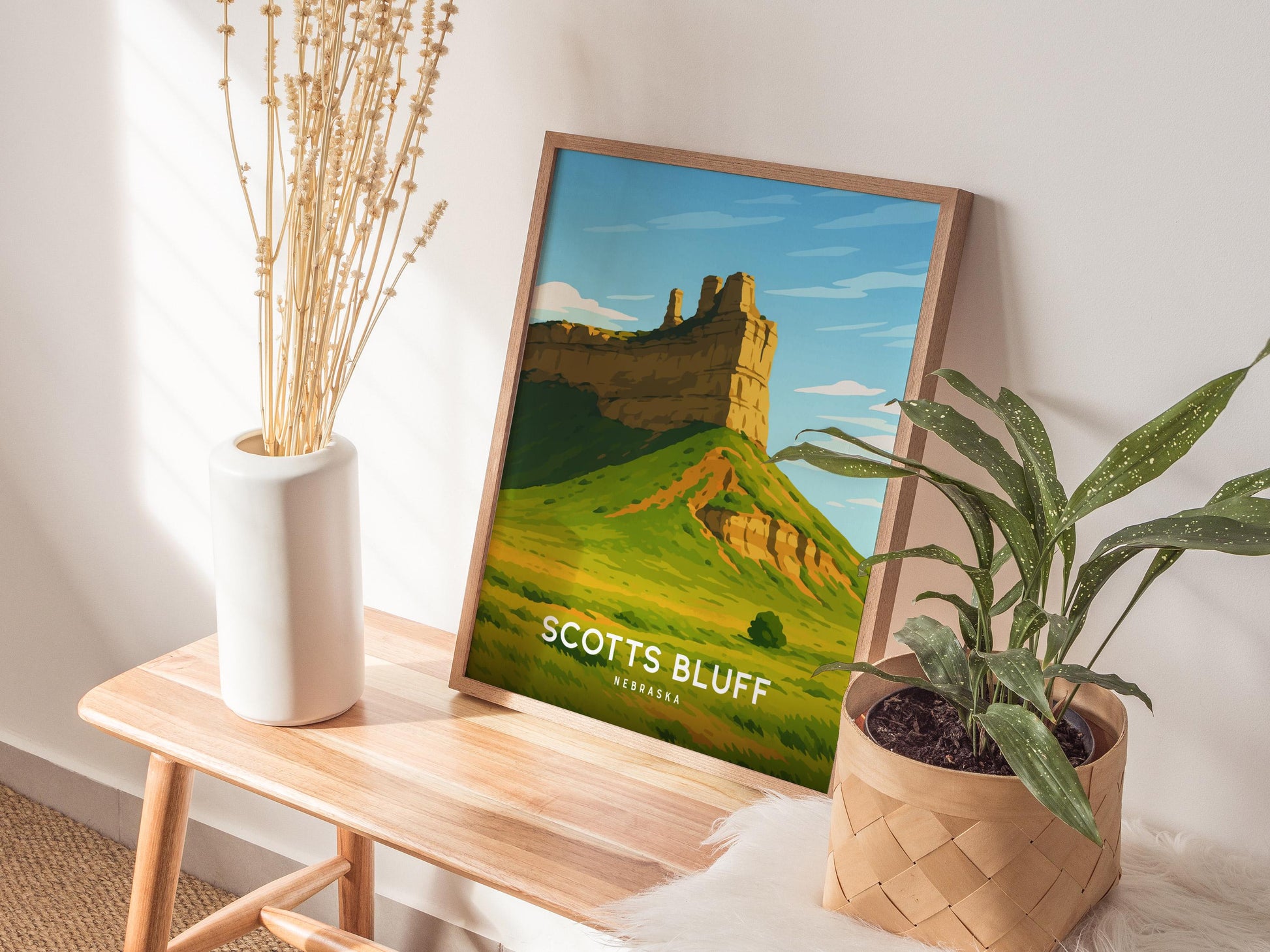 Framed poster of Scotts Bluff National Monument on a wooden table with plants and a vase.