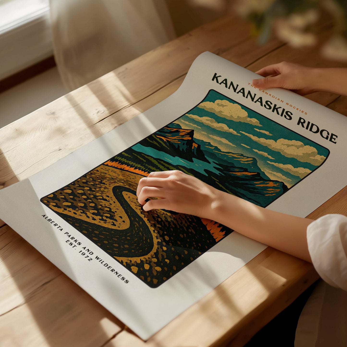 Person holding a poster of Kananaskis Ridge with scenic design on a wooden table.