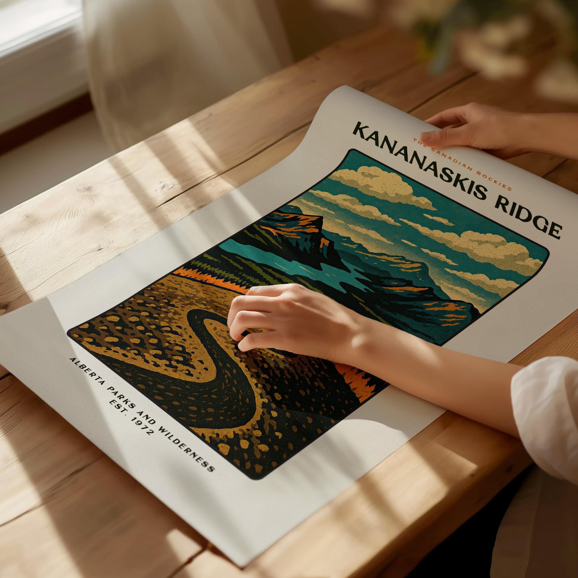 Person holding a poster of Kananaskis Ridge with scenic design on a wooden table.