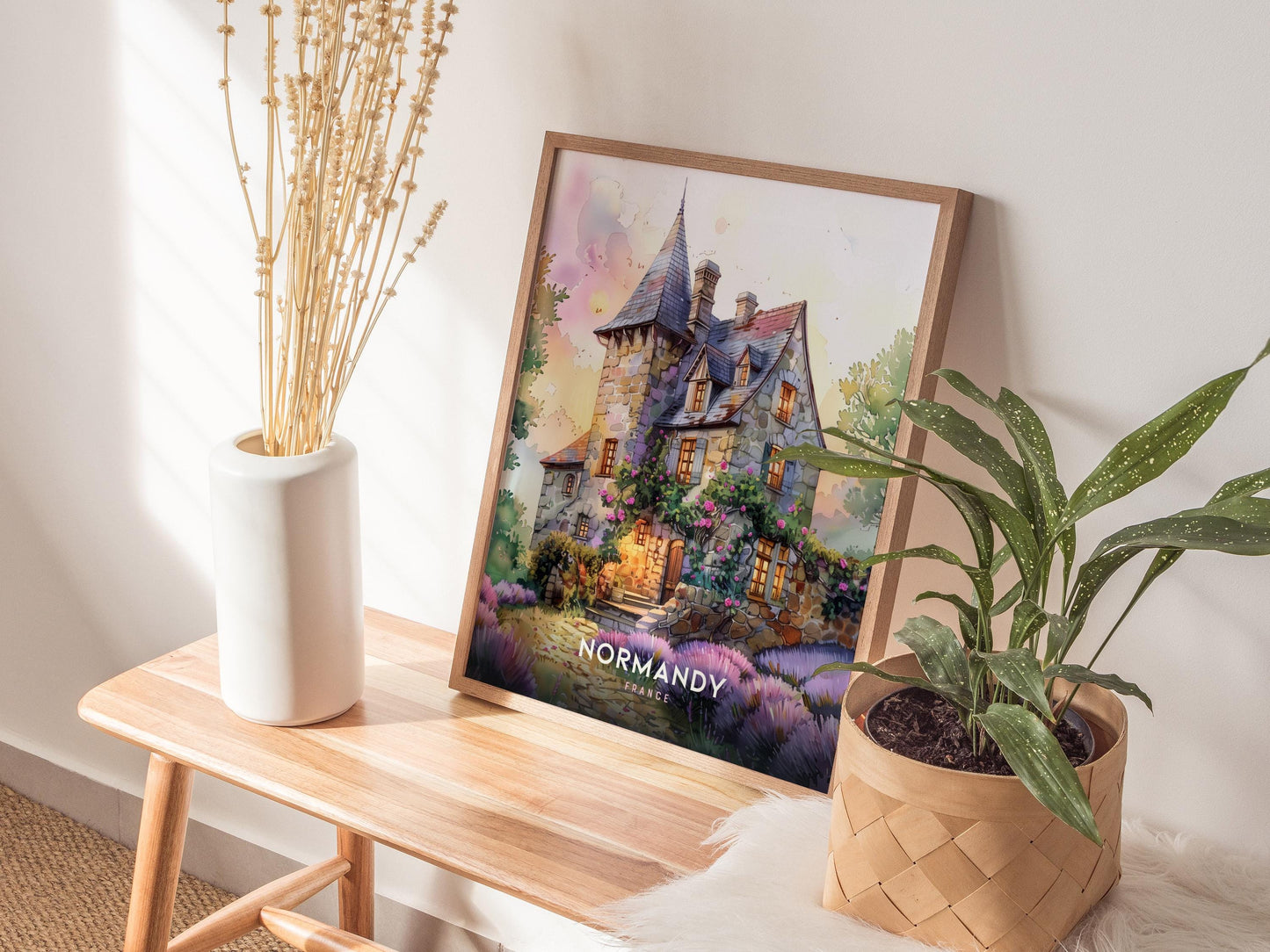 Framed artwork of a house labeled 'Normandy' on a wooden table with plants and decor.