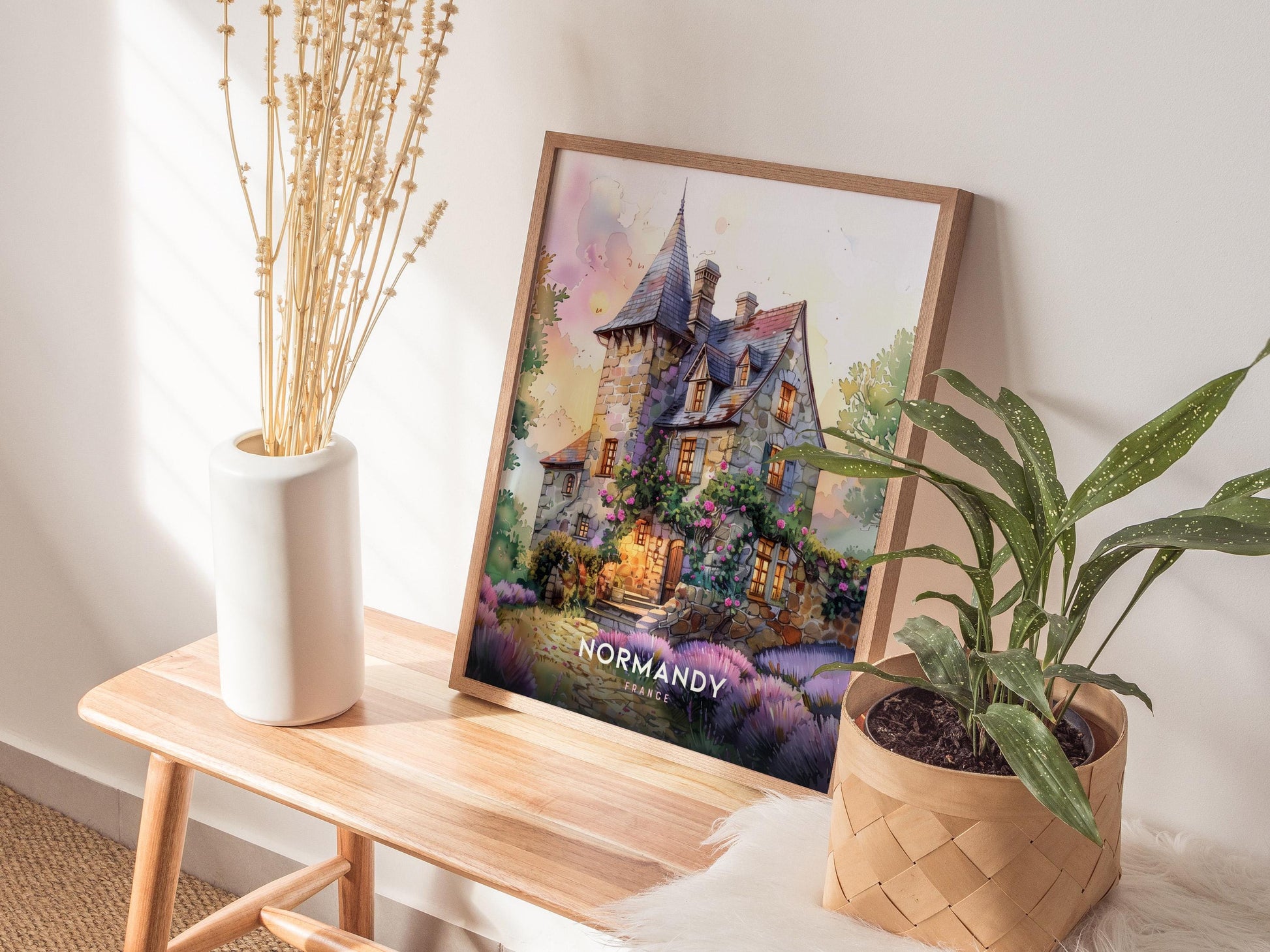 Framed artwork of a house labeled 'Normandy' on a wooden table with plants and decor.