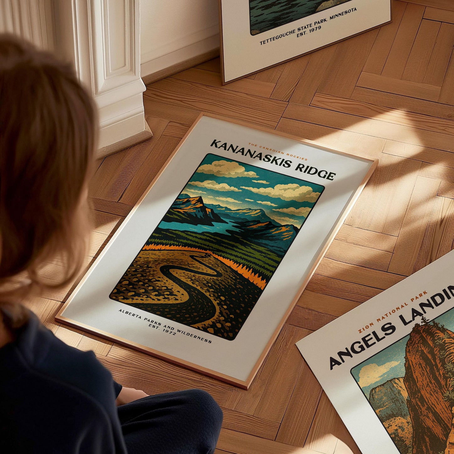 Person looking at a framed poster of Kananaskis Ridge on a wooden floor.