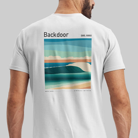 A man is wearing a white t-shirt featuring a colorful graphic of a wave and beach scene on the back. The words Backdoor and Oahu, Hawaii are printed above the image, capturing a coastal vibe.
