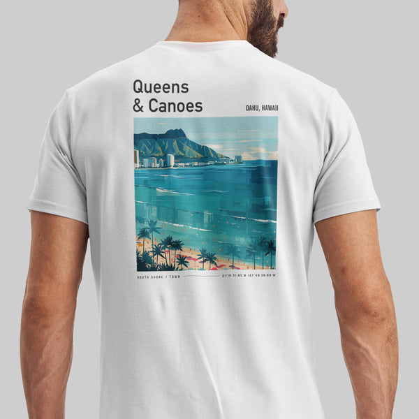 A man wears a white T-shirt featuring a vintage-style illustration of Waikiki Beach on the back, with text reading Queens & Canoes and Oahu, Hawaii. The design includes a scenic view of the ocean, palm trees, and distant buildings.