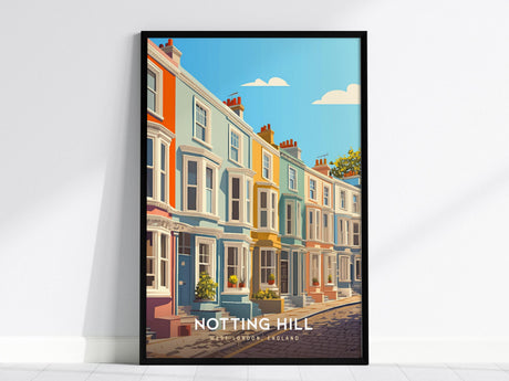 A framed poster depicts a row of colorful, pastel townhouses along a cobblestone street under a blue sky with clouds. The artwork is titled Notting Hill and rests against a white wall.