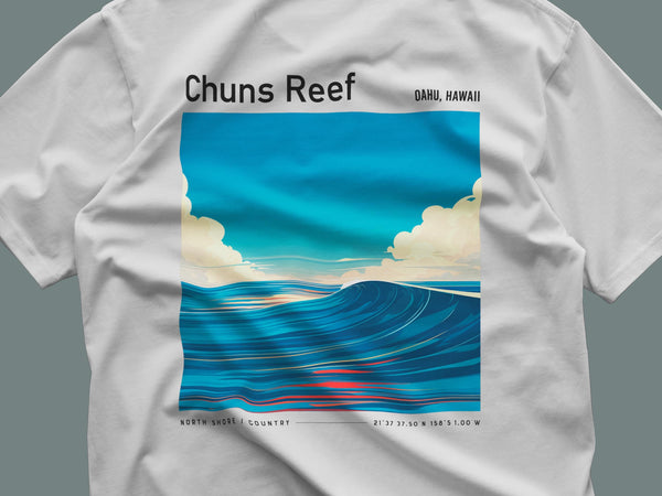 A white T-shirt featuring a vibrant illustration of ocean waves with fluffy clouds and a bright blue sky, labeled Chuns Reef Oahu, Hawaii. The design captures a serene coastal scene, reflecting a relaxed, tropical vibe.