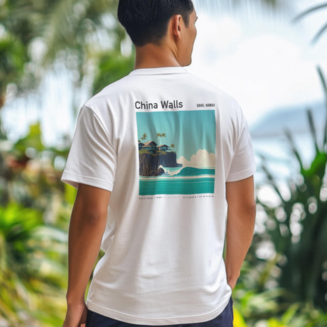 A person wearing a white T-shirt with a colorful graphic on the back depicting a tropical coastline, featuring palm trees and waves. The shirt reads China Walls Oahu, Hawaii and is set against a blurred, lush background.