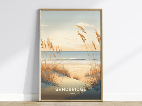 A framed poster features an illustration of a serene beach scene with coastal dunes and tall grasses under a pastel sunrise sky. The ocean waves gently roll in the background, and the word Sandbridge is written at the bottom.