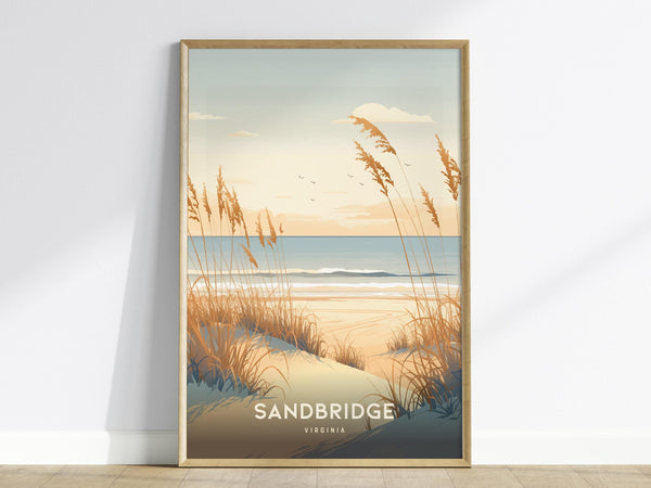 A framed poster features an illustration of a serene beach scene with coastal dunes and tall grasses under a pastel sunrise sky. The ocean waves gently roll in the background, and the word Sandbridge is written at the bottom.