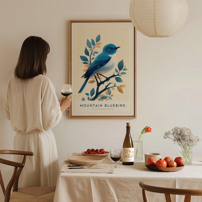 Woman in a white dress standing in a dining room with a framed artwork of a mountain bluebird.