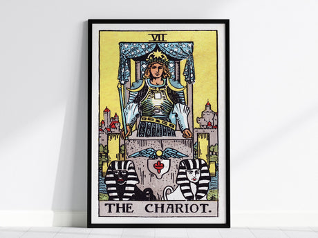 The image shows a framed poster of The Chariot tarot card from the Rider Waite deck, featuring a figure in armor with a crown, holding a wand, and two sphinxes at the base. The background is a vibrant yellow.