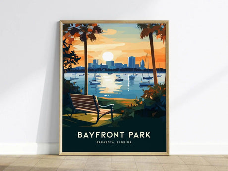 This illustrated poster features a sunset view over Sarasota Bay with sailboats on the water, a bench in the foreground, and palm trees framing the scene. The text Bayfront Park Sarasota, Florida is displayed at the bottom.