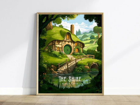 A framed poster depicting a Hobbit house with a round door, nestled under green hills, with a stone path and lush garden in a tranquil countryside setting.