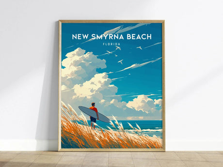 A framed poster titled New Smyrna Beach, Florida features a vibrant illustration of a surfer standing on a grassy dune, gazing at the ocean under a bright blue sky filled with fluffy clouds and seagulls.