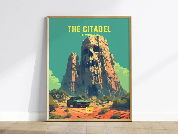 The image shows a framed poster of The Citadel from Mad Max, featuring a towering rock formation with a skull carving. A car is visible on the arid landscape, under a clear blue sky.