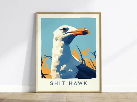 A framed poster features a stylized seagull with an orange beak against a blue and orange abstract background, titled Shit Hawk. It rests on a wooden floor.