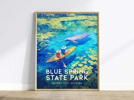 A framed poster shows two kayakers in colorful attire paddling on vibrant blue waters with a manatee nearby, surrounded by yellow lily pads.