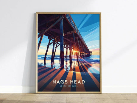 A framed poster depicts a vibrant sunset behind a pier, casting long shadows over the water. The text Nags Head, North Carolina is displayed at the bottom.