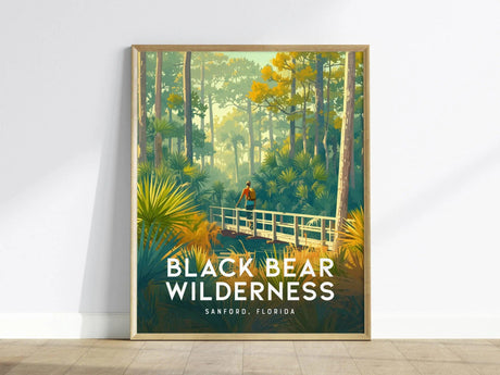 A framed poster depicts a hiker on a wooden bridge amidst dense greenery and tall trees, titled Black Bear Wilderness, Sanford, Florida.