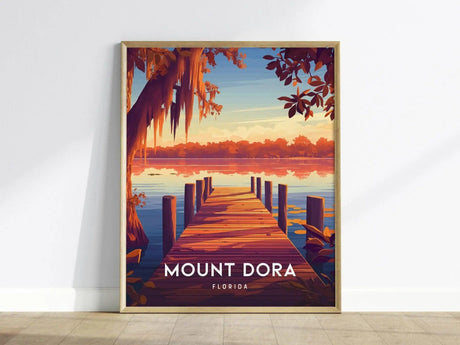 A framed poster depicting a wooden pier extending into a serene lake at sunset, surrounded by vibrant orange foliage, with Mount Dora, Florida text at the bottom.