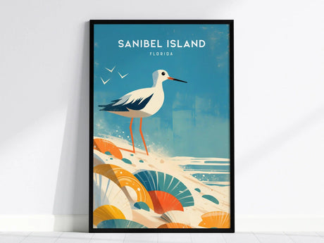A framed poster of Sanibel Island, Florida, featuring a sandpiper with long legs standing on a beach with colorful seashells and gentle waves under a blue sky.