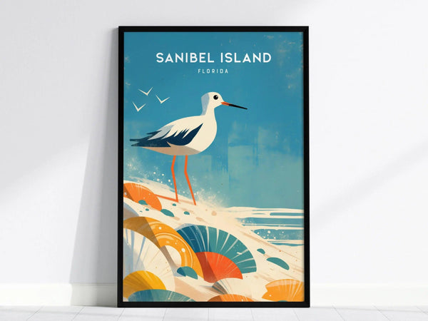 A framed poster of Sanibel Island, Florida, featuring a sandpiper with long legs standing on a beach with colorful seashells and gentle waves under a blue sky.