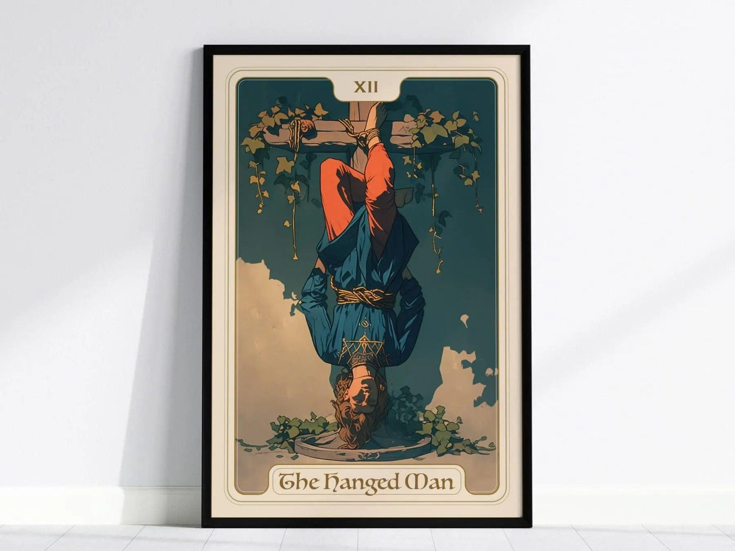 A framed poster of the Hanged Man Tarot card, featuring a figure suspended upside down from a tree, dressed in blue and red clothing. The illustration includes green vines, conveying themes of surrender and enlightenment.