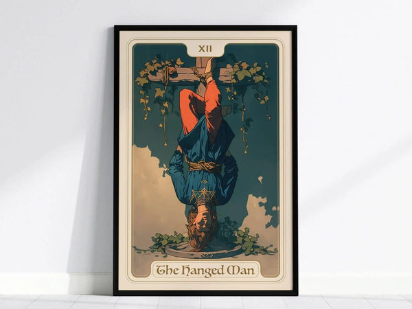 A framed poster of the Hanged Man Tarot card, featuring a figure suspended upside down from a tree, dressed in blue and red clothing. The illustration includes green vines, conveying themes of surrender and enlightenment.