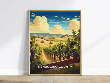 Framed poster of Mendocino County featuring a vineyard with lush grapevines, rolling hills, and a vibrant sky, leaning against a white wall on a wooden floor.