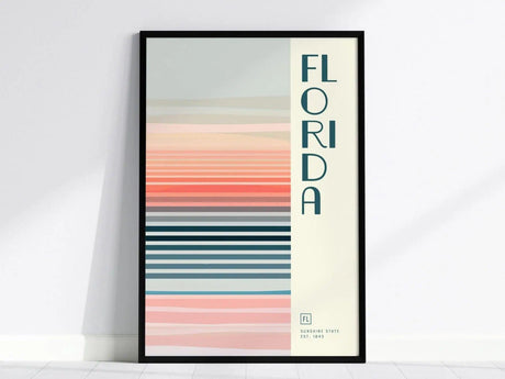 A framed poster with vertical text reading FLORIDA alongside horizontal pastel stripes in pink, blue, and beige tones, evoking a minimalist design. The bottom reads Sunshine State Est. 1845.
