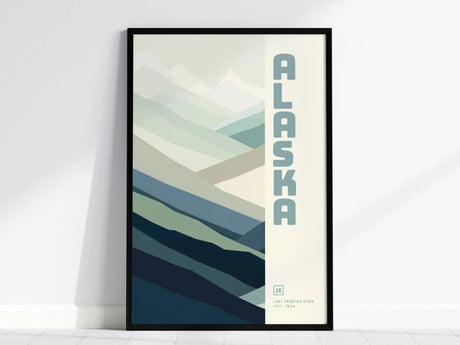 Framed poster featuring a minimalist abstract design of layered mountains in shades of blue and gray, with ALASKA vertically written on the right.