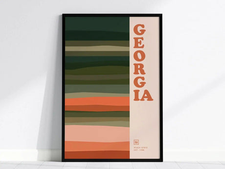Framed poster featuring the word GEORGIA in bold orange letters, with horizontal earthy stripes in various shades of green and peach, evoking a minimalist design.