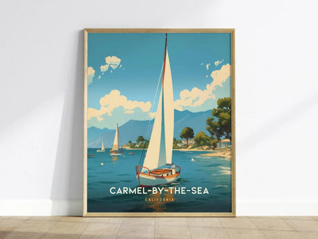 A framed poster of Carmel-by-the-Sea shows a sailboat on blue waters, surrounded by trees and distant mountains under a partly cloudy sky.