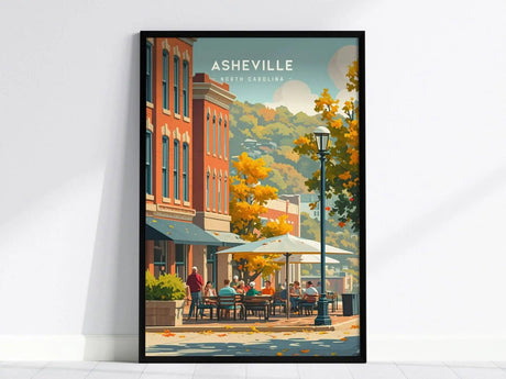 A framed poster depicting Asheville, North Carolina, features vibrant autumn colors, outdoor cafés, and historic buildings against a backdrop of the Blue Ridge Mountains.