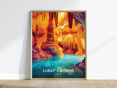 A vibrant poster of Luray Caverns featuring colorful flowstone formations and a serene blue pool, framed in a simple wooden frame, leaning against a white wall.