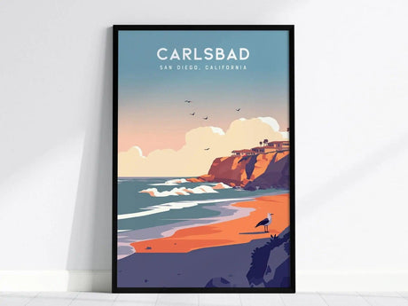 Framed poster depicting Carlsbad, California, with vibrant cliffs, sandy beach, and ocean waves under a pastel sky. A seagull stands on the shore, enhancing the coastal scenery.