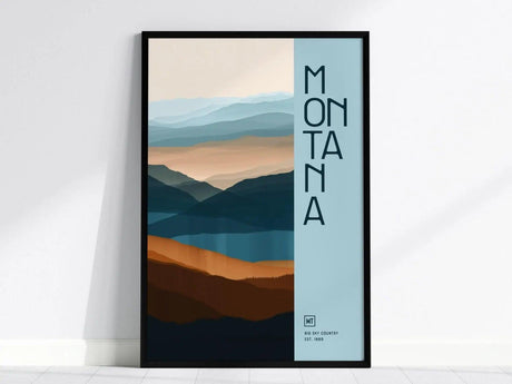 Minimalist poster featuring layered mountain silhouettes in blue and orange tones with Montana text on the side. Framed artwork leans against a white wall for modern decor.