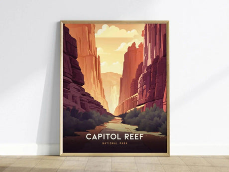 Framed poster of Capitol Reef National Park featuring stylized red rock canyons, dramatic cliffs, and a sunlit sky, leaning against a white wall on a wooden floor.