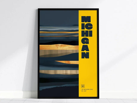 A framed Michigan poster features bold typography on a bright yellow strip, alongside abstract dark and gold landscape patterns. The text reads The Wolverine State Est. 1837.