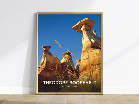 Framed poster of Theodore Roosevelt National Park features illustrated hoodoos under a bright blue sky, with tall grasses in the foreground.