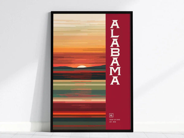 A framed minimalist poster featuring abstract horizontal lines in warm hues with the word Alabama in bold letters on the right. The sun sets behind a stylized landscape.