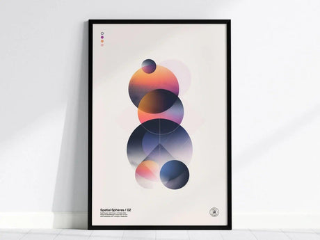 A framed modern abstract art poster featuring overlapping geometric spheres with gradient transitions in pink, orange, and blue tones, leaning against a white wall.