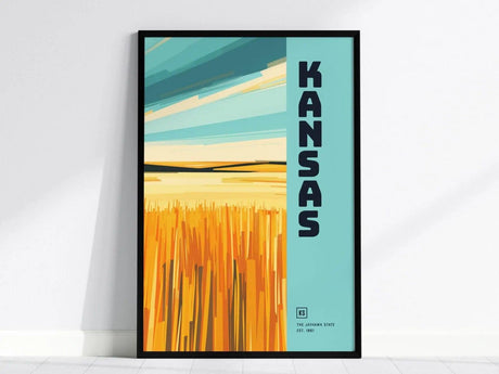 A framed poster featuring stylized golden wheat fields under a blue sky with KANSAS in bold letters on the right. The design is modern and vibrant.