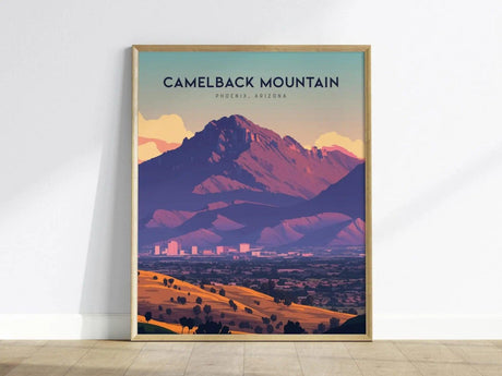 A framed poster of Camelback Mountain in Phoenix, Arizona, features vibrant desert tones and a dramatic silhouette, with a cityscape below under a colorful sky.