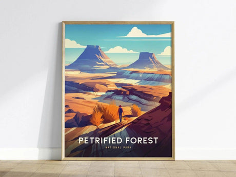 A colorful poster of Petrified Forest National Park features a lone figure overlooking vibrant desert badlands and mesas under a bright blue sky, framed in light wood.