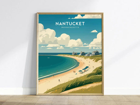 A framed poster of Nantucket, Massachusetts, features a scenic beach with umbrellas, cottages, and a vast ocean under a partly cloudy sky, leaning against a white wall.